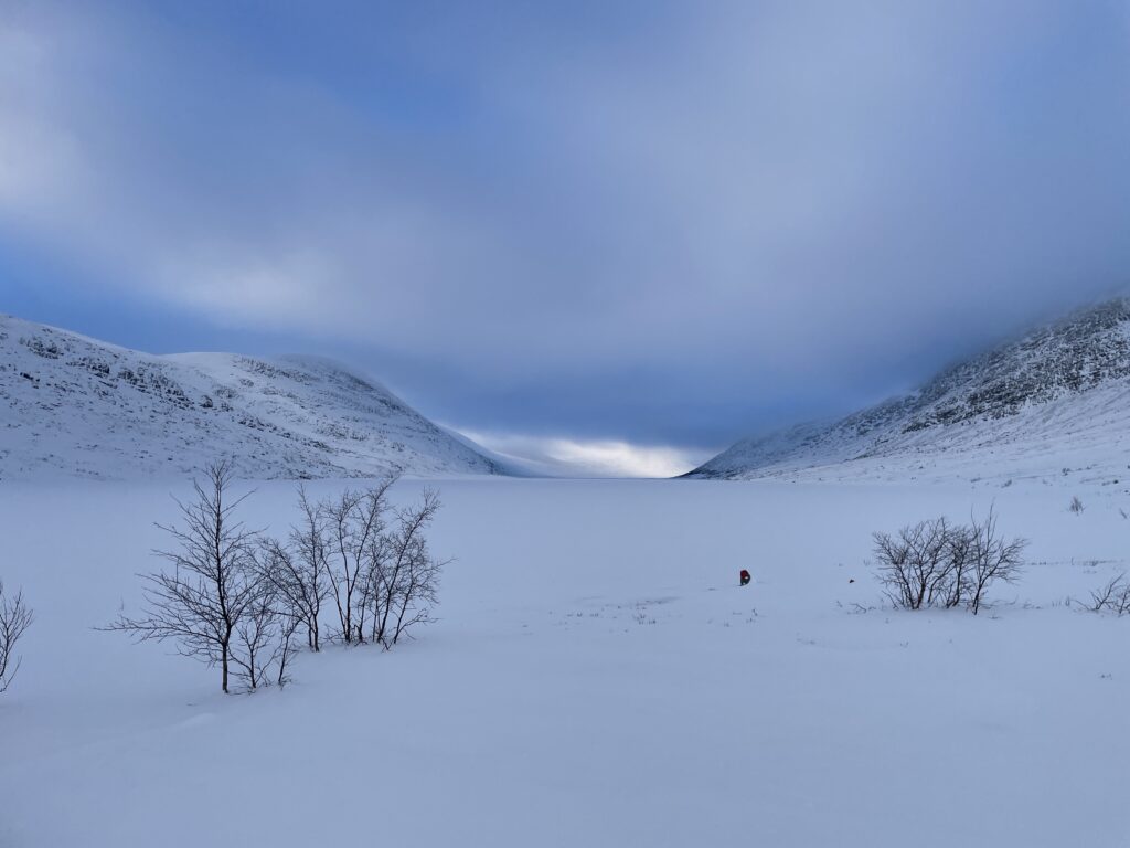 Zugeschneiter See zwischen zwei Bergen auf einer Schneemobiltour.